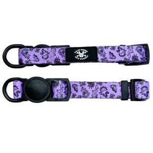 May include: A light purple pet collar featuring a black graphic print of various animals and butterflies. The collar includes a black plastic buckle, a black metal D-ring, and a black rectangular fabric label with the text TUFF BONES PET SUPPLY.