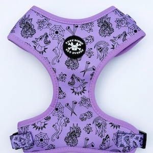 May include: A light purple pet harness featuring a black line art pattern of skulls, roses, spiderwebs, dice, and howling dogs. A circular black patch in the center displays a white bulldog graphic and the text Tuff Bones Pet Supply.