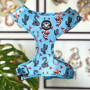 May include: A blue dog harness with a western-themed print featuring cacti, snakes, horseshoes, and skulls. The harness has a Tuffy Bones Pet Supply logo.