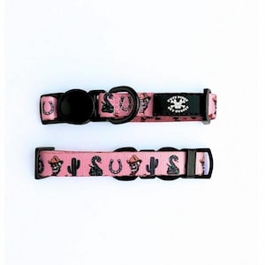 May include: Two pink dog collars with black hardware. The collars feature a repeating pattern of cowboy hats, cacti, horseshoes, and snakes. One collar has a black label with the text "TUFF BONES PET SUPPLIES".