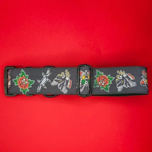 May include: A dark gray pet collar featuring a repeating pattern of traditional tattoo-style illustrations including red roses with green leaves, barbed wire, eagles, and colorful moths, equipped with black plastic buckles and metal D-rings.