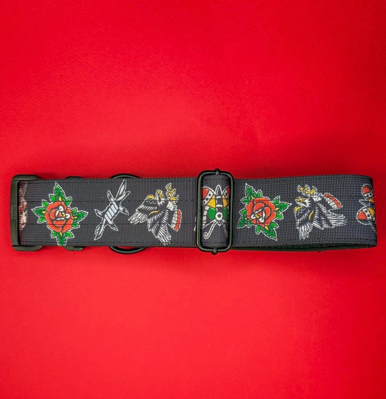 May include: A dark gray pet collar featuring a repeating pattern of traditional tattoo-style illustrations including red roses with green leaves, barbed wire, eagles, and colorful moths, equipped with black plastic buckles and metal D-rings.