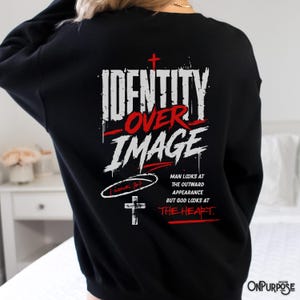 Pu&ograve; includere: Una felpa nera a maniche lunghe con testo grafico bianco e rosso sul retro che recita "IDENTITY OVER IMAGE" con una piccola croce, un riferimento a "1 SAMUEL 16:7" e il testo "MAN LOOKS AT THE OUTWARD APPEARANCE BUT GOD LOOKS AT THE HEART."