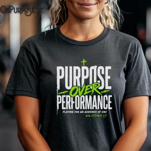 May include: A charcoal gray short-sleeve t-shirt featuring the white and lime green text "PURPOSE OVER PERFORMANCE" with a small cross icon, the phrase "PLAYING FOR AN AUDIENCE OF ONE," and the citation "GALATIANS 1:10" printed on the front.