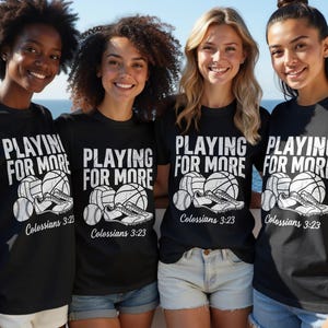 May include: Four women wearing black t-shirts with the text "PLAYING FOR MORE" in white. The shirts feature illustrations of sports equipment, including baseballs, volleyballs, basketballs, and running shoes. The text "Colossians 3:23" is also printed on the shirts.