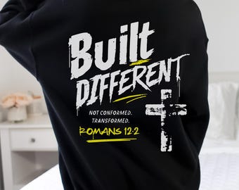 May include: A black long-sleeve sweatshirt featuring white and yellow graphic text on the back that reads Built Different, Not Conformed. Transformed. Romans 12:2, accompanied by a white cross graphic with a distressed, paint-like texture.