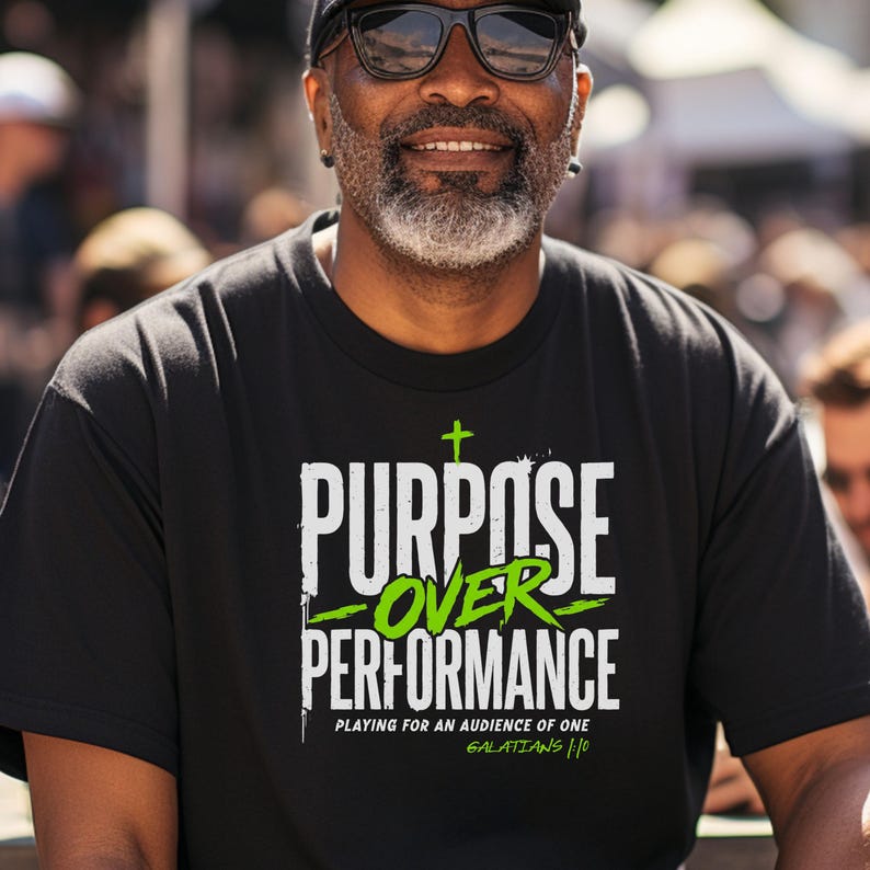 May include: A black t-shirt featuring the white and lime green text "PURPOSE OVER PERFORMANCE" with a small cross icon above the word "PURPOSE". Below the main text, it reads "PLAYING FOR AN AUDIENCE OF ONE" and "GALATIANS 1:10" in smaller font.