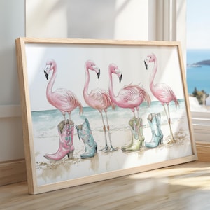May include: A framed print of five pink flamingos wearing cowboy boots. The flamingos are standing on a beach with blue water in the background.