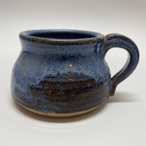 May include: A blue and brown ceramic mug with a rounded body and a handle. The mug has a speckled glaze with a dark brown band around the bottom.