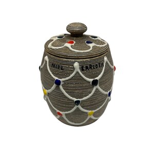 May include: A ceramic jar with a lid, featuring a textured brown surface and white decorative accents. The jar is adorned with colorful dots and the text "MIEL CARIOTA". The lid has a knob on top. This item is suitable for kitchen decor.