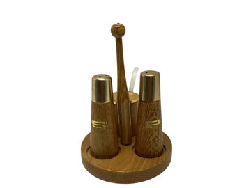 May include: A vintage wooden salt and pepper shaker set with a matching toothpick holder and spoon. The shakers have gold-colored metal tops and a gold-colored label. The set sits on a round wooden base.