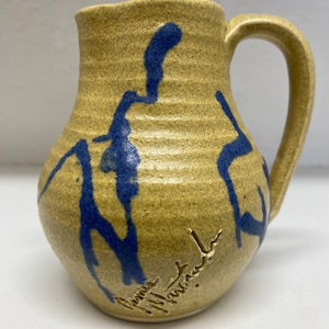 May include: A yellow ceramic pitcher with blue abstract designs and a handwritten signature on the bottom.