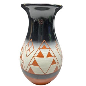 May include: A ceramic vase with a black top that fades to white and orange geometric designs. The vase has a wide mouth and a rounded body, with a gray and orange base. The design features triangles and diamond shapes.