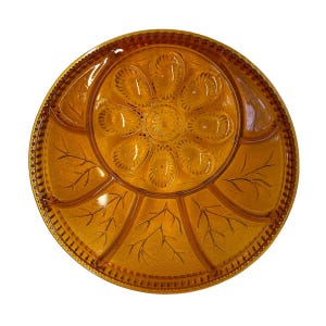 May include: Amber-colored glass serving platter with a floral and leaf design. The round platter features a central flower-like pattern surrounded by petal-shaped compartments. The outer rim has a beaded edge.