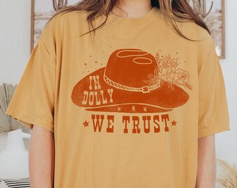 May include: A mustard yellow t-shirt with a red graphic of a cowboy hat with flowers and the text "In Dolly We Trust".
