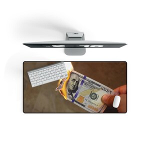 Pode incluir: Um rato de computador e um teclado estão em uma mesa com uma nota de US$ 100 em chamas. A nota está sendo segurada por uma mão.