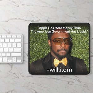 May include: Black mousepad with a quote by will.i.am: "Apple Has More Money Than The American Government Has Liquid." The mousepad features a photo of will.i.am wearing sunglasses and a gold bow tie. A white keyboard is visible in the background.