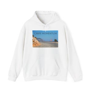 May include: White hoodie with a front pocket and drawstring. The front features a rectangular image of a road winding along a coastline, with the text "CARPE MOMENTUM" above the image.