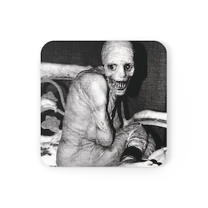 May include: Square coaster featuring a black and white image of a pale, emaciated figure with a gaunt face and a wide, toothy grin. The figure is seated, with its arms and legs bent. The background is a dark, textured wall.