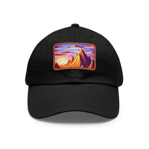May include: Black baseball cap with a brown patch featuring a colorful mountain landscape with a sunset.