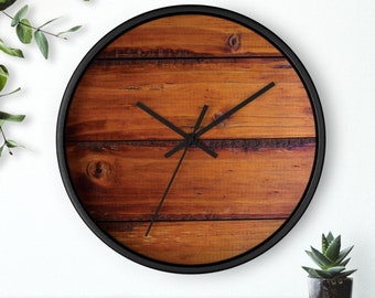 May include: A round wall clock with a black frame. The clock face features a wood grain design in shades of brown. Black clock hands indicate the time. The clock is a decorative item for home decor.
