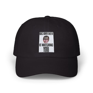 May include: Black baseball cap with a curved brim. The cap features an embroidered patch with the text "BIG BROTHER IS WATCHING YOU" and a portrait of a man's face.