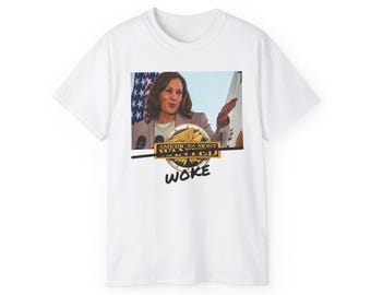 May include: White t-shirt featuring an image of a woman speaking at a podium. The image includes the text "AMERICA'S MOST WANTED" above the word "WOKE" in a gold and black design. The background includes an American flag.