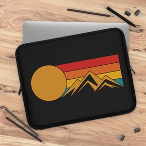 Pode incluir: Capa para laptop preta com um design de pôr do sol retrô com um sol amarelo e montanhas na frente de um fundo listrado multicolorido.