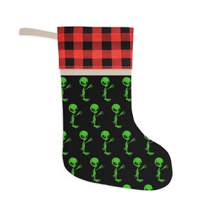 May include: A black Christmas stocking with a red and black buffalo plaid cuff. The stocking features a repeating pattern of green aliens.