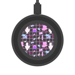 Puede incluir: Un cargador inalámbrico negro con un diseño retro de los años 80. El centro presenta un patrón de cuadrícula con delfines, bustos, computadoras y otros gráficos en rosa, morado y blanco. Un cable USB negro se extiende desde la parte superior.