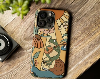 May include: A phone case with a whimsical illustration. The design features a green frog playing a mandolin while sitting on a skull atop a snail. The background includes a sun, flowers, and a stylized eye, all in a retro color palette.