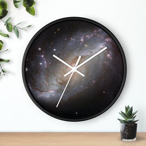 May include: A black clock with a white face and hands. The clock face features a photo of a galaxy with a spiral pattern.