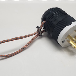 May include: A black and white electrical plug with a gray and orange rope attached. The plug has three prongs and a white plastic housing.