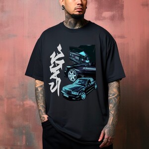 Puede incluir: Camiseta negra con un gráfico de un coche clásico en negro y verde azulado. La camiseta tiene caracteres japoneses blancos en el lado izquierdo. El diseño muestra tres vistas diferentes del coche.