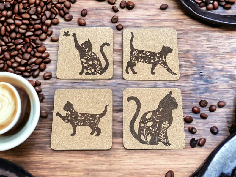 May include: Set of four brown cork coasters with black silhouette images of cats with floral designs. The cats are in different poses, including sitting, standing, and lying down.