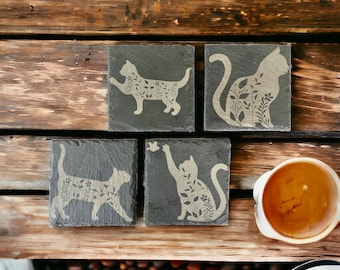 May include: Four black slate coasters with a white silhouette of a cat with floral details on each coaster.