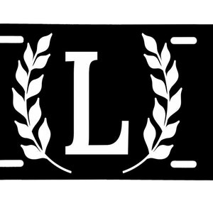 May include: Black license plate with a white letter L surrounded by a wreath of leaves.