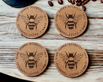 May include: Four cork coasters with a bee design and the text "KIND HAPPY YOURSELF TRUE HUMBLE SWEET THANKFUL" around the edge of each coaster.