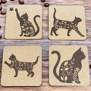 May include: Set of four cork coasters featuring a silhouette of a cat with floral designs. Each coaster has a different pose of the cat.