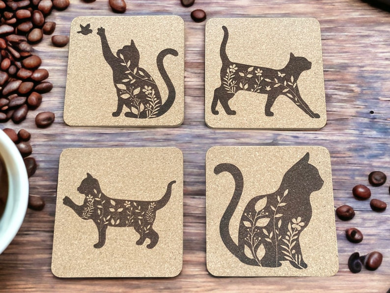 May include: Set of four cork coasters featuring a silhouette of a cat with floral designs. Each coaster has a different pose of the cat.