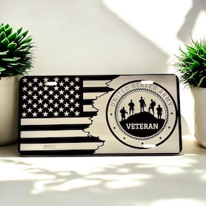 May include: A silver metal license plate with a distressed American flag design and a black and white seal that reads "United States Army Veteran".
