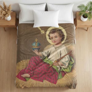 Plush blanket featuring a vintage religious illustration of a cherub with a halo holding a globe and paintbrush, draped on a bed with white pillows and wooden nightstands