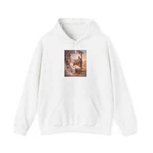 White unisex hoodie with a nativity scene print centered on the chest, depicting Mary, Joseph, and baby Jesus in a stable with warm golden lighting