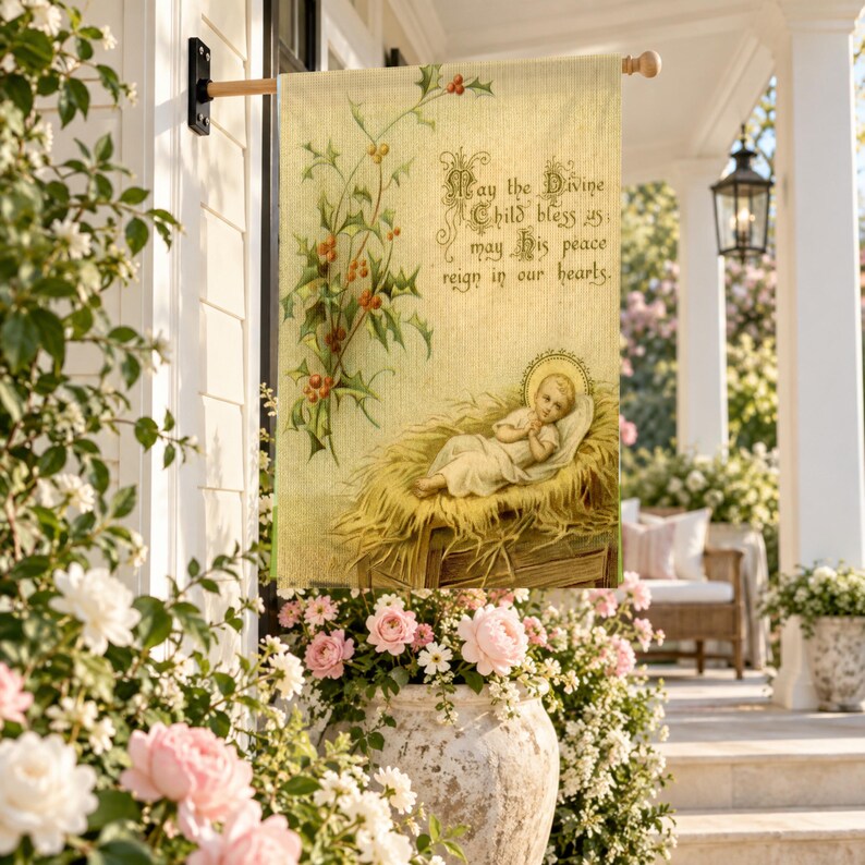 Nativity garden flag in the large size, hung from a wall pole over a porch with pink peonies