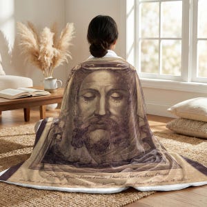 Holy Face plush blanket wrapped around a woman's shoulders as she sits on the floor