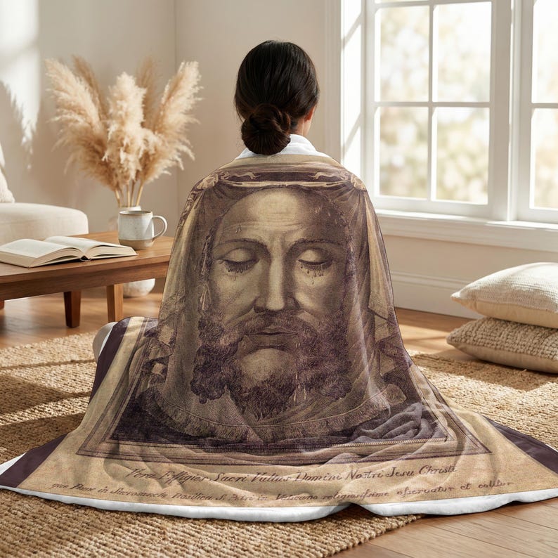 Holy Face plush blanket wrapped around a woman's shoulders as she sits on the floor
