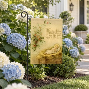 Nativity garden flag on a garden stand among blue and white hydrangeas beside a front walk