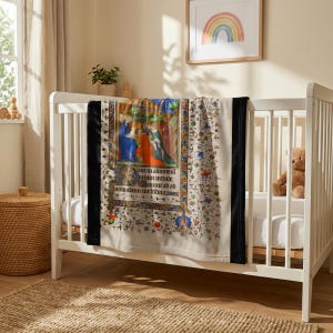 Nativity plush blanket hung over the rail of a white crib with a teddy bear inside