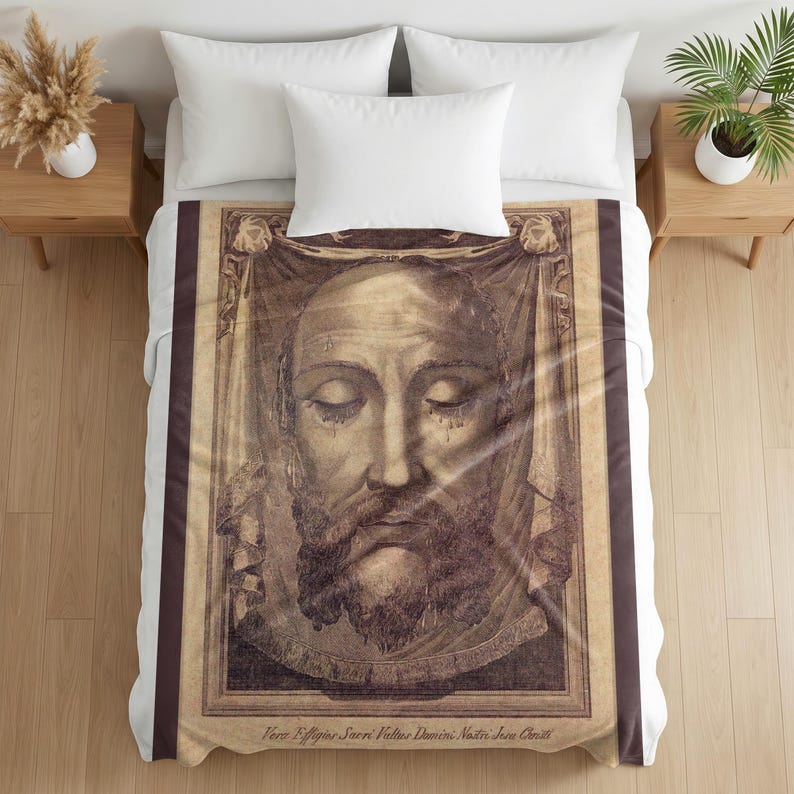 Plush blanket featuring a sepia-toned engraved portrait of the Holy Face with closed eyes and beard, displayed on a bed with white pillows and wooden nightstands