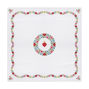 Puede incluir: Un paño cuadrado blanco con una corona central de rosas rojas, rosas y nomeolvides azules que rodea un emblema rojo del Sagrado Corazón. El borde consiste en una guirnalda floral continua de flores rojas, rosas y amarillas.